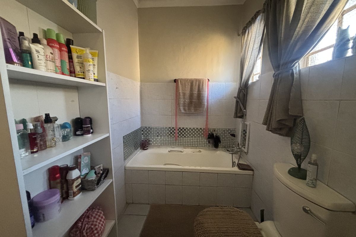 A functional bathroom featuring a built-in bathtub with tiled surround, a standard toilet, and built-in shelving for storage.
