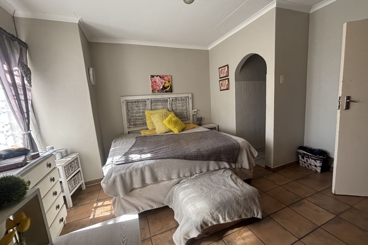 A bedroom featuring tiled flooring and an arched entryway leading to an adjoining space, finished with neutral wall tones and cove cornicing.