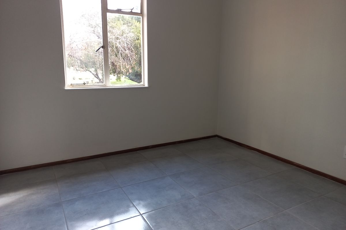 An empty bedroom featuring neutral wall finishes, tiled flooring, and a window providing natural light.