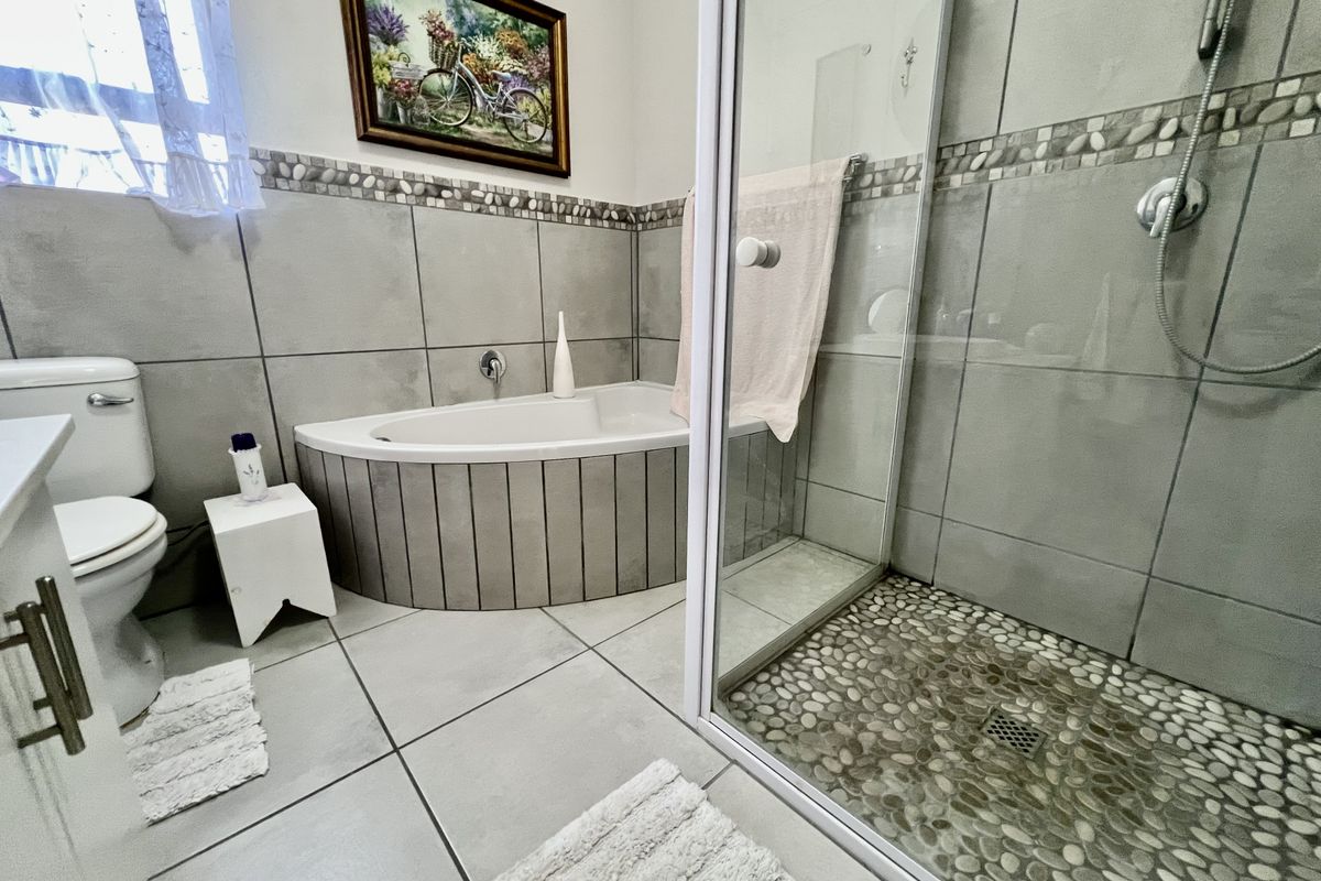 A well-maintained bathroom featuring a corner bathtub, a separate walk-in shower with a pebble floor, and neutral ceramic wall tiling.