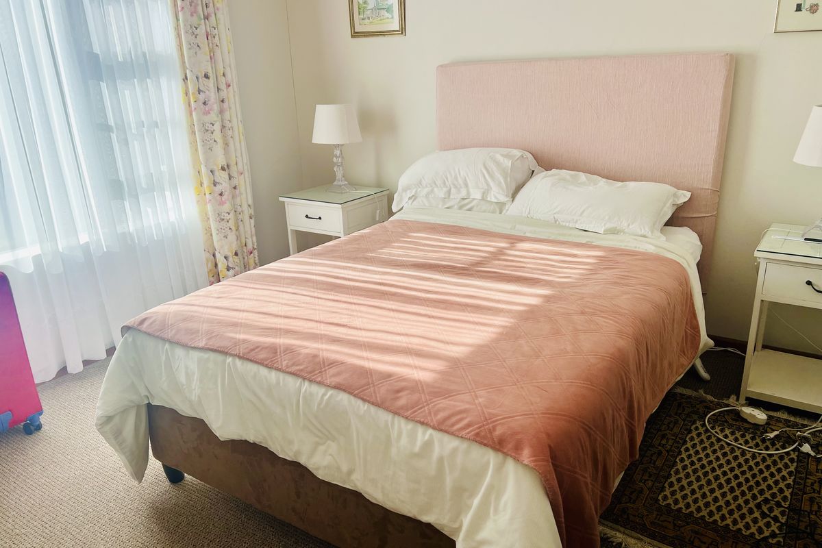A cozy bedroom featuring neutral walls, carpeted flooring, and natural light filtering through window treatments.