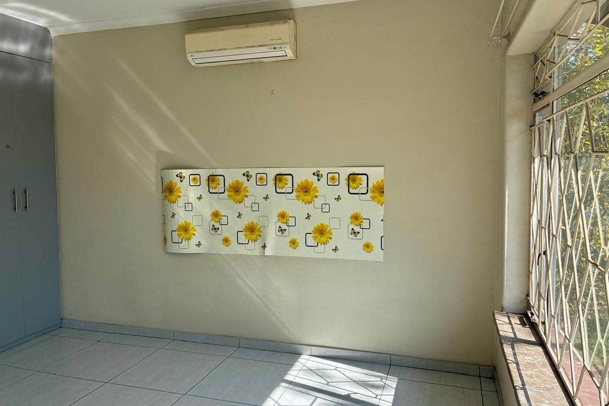 An empty bedroom featuring tiled flooring, a built-in wardrobe, and a wall-mounted air conditioning unit, with security bars installed on the window.
