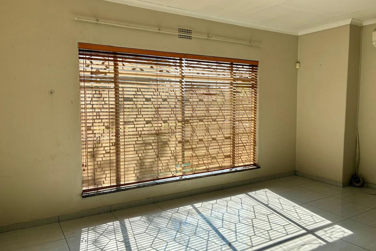 An empty living room featuring tiled flooring, coved ceilings, and large windows fitted with wooden venetian blinds.