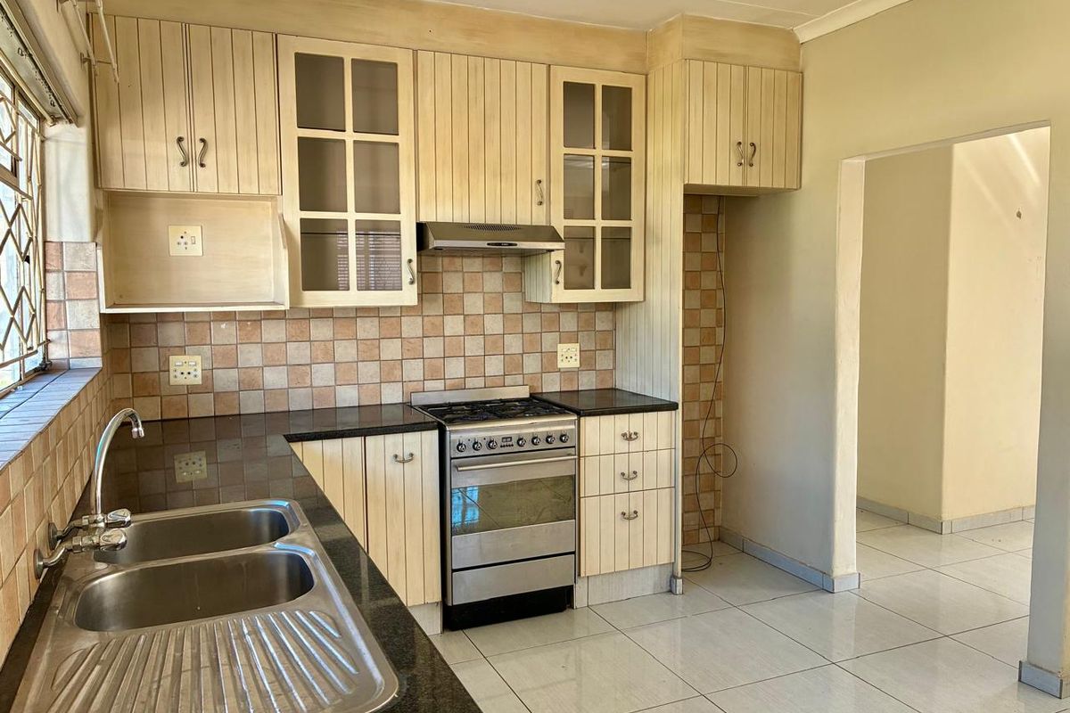 A functional kitchen featuring granite countertops, a double stainless steel sink, built-in cabinetry, and a freestanding stove with an extractor fan.