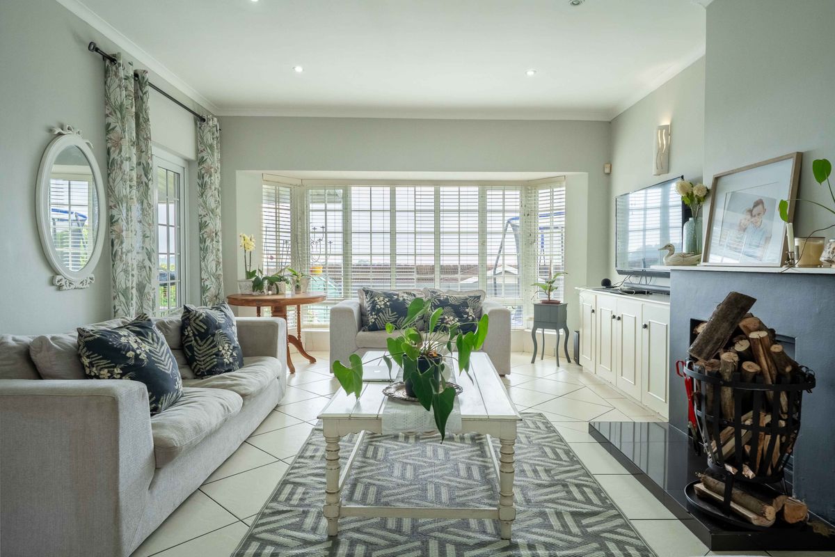 A bright and inviting living room featuring a large bay window with plantation shutters, tiled flooring, and a cozy fireplace with built-in cabinetry.