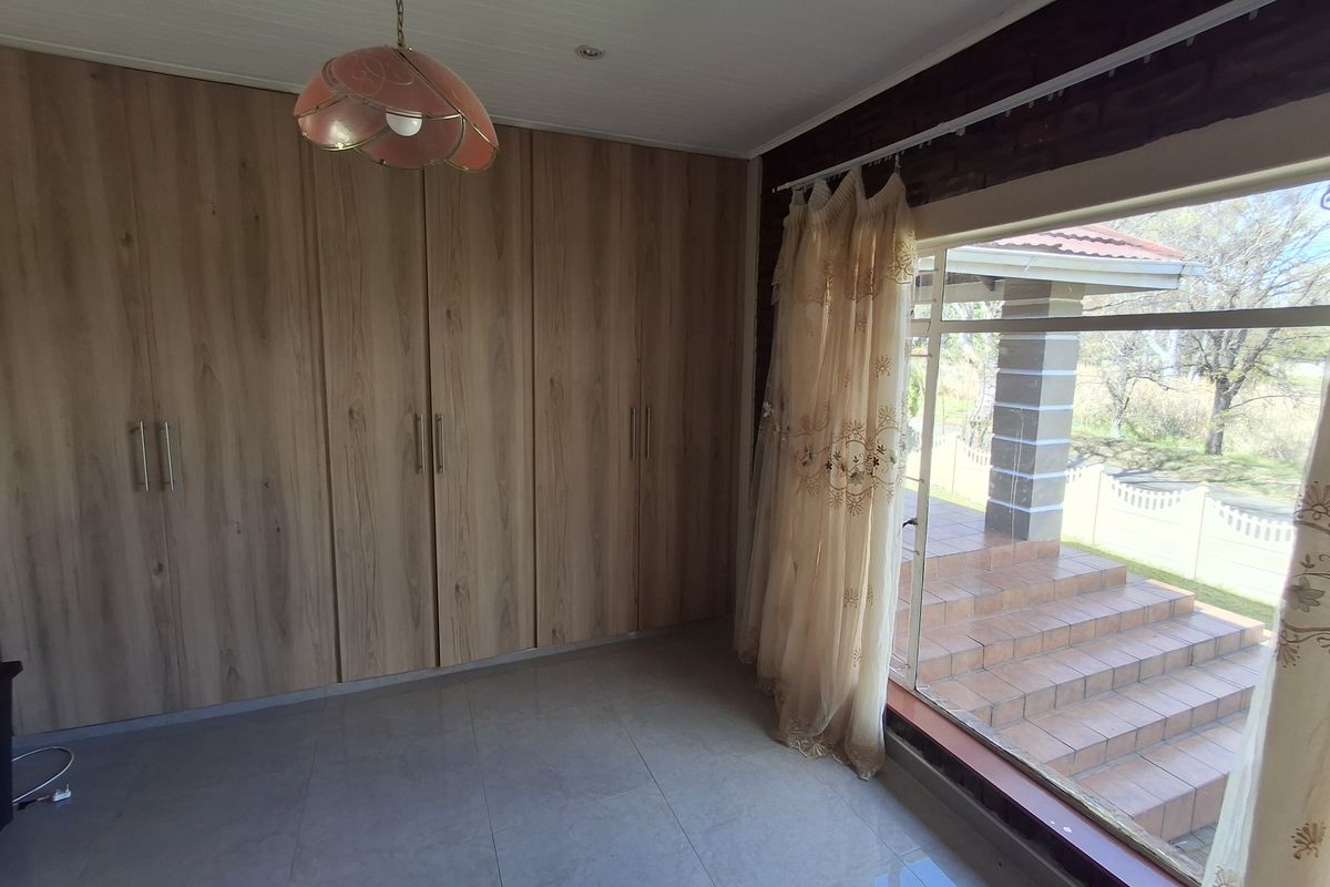 A bright, empty bedroom featuring modern wood-finish built-in cupboards, tiled flooring, and a large sliding door providing direct access to the outdoor patio area.