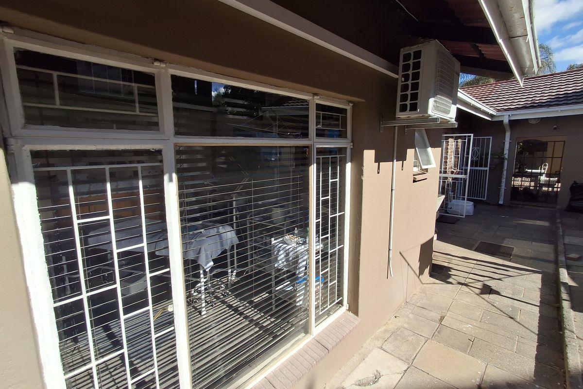 Rear exterior view of the property featuring a paved walkway, security bars on windows, and an external air conditioning unit.