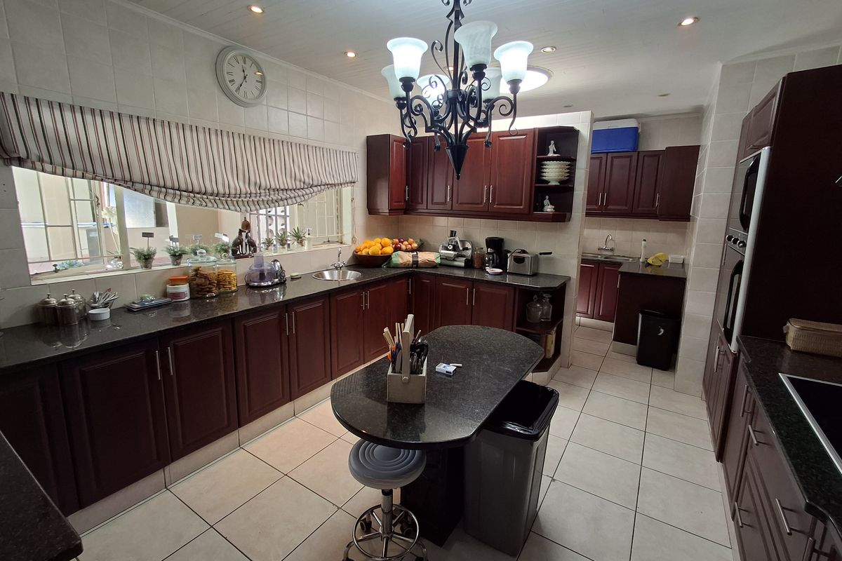 Spacious kitchen featuring dark wood cabinetry, granite countertops, a central island, and a separate scullery area with integrated appliances.