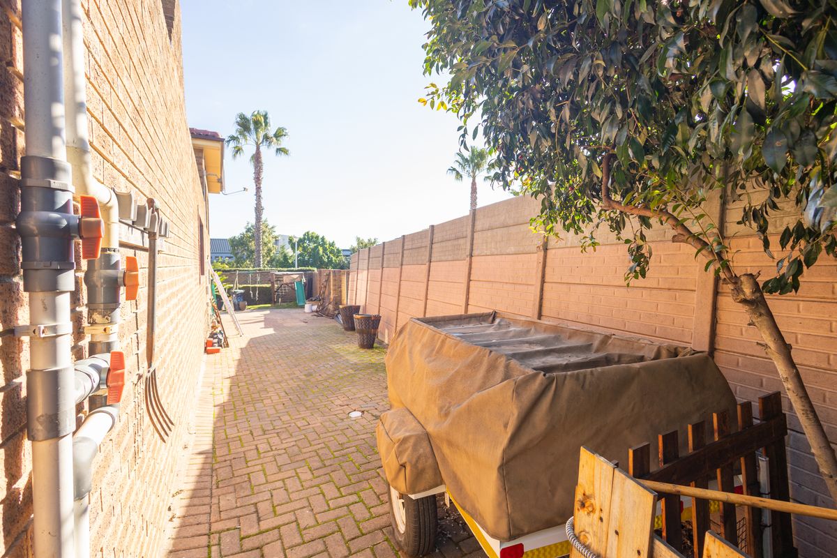 A side passage of the property featuring brick paving, a precast concrete boundary wall, and exposed external plumbing infrastructure.