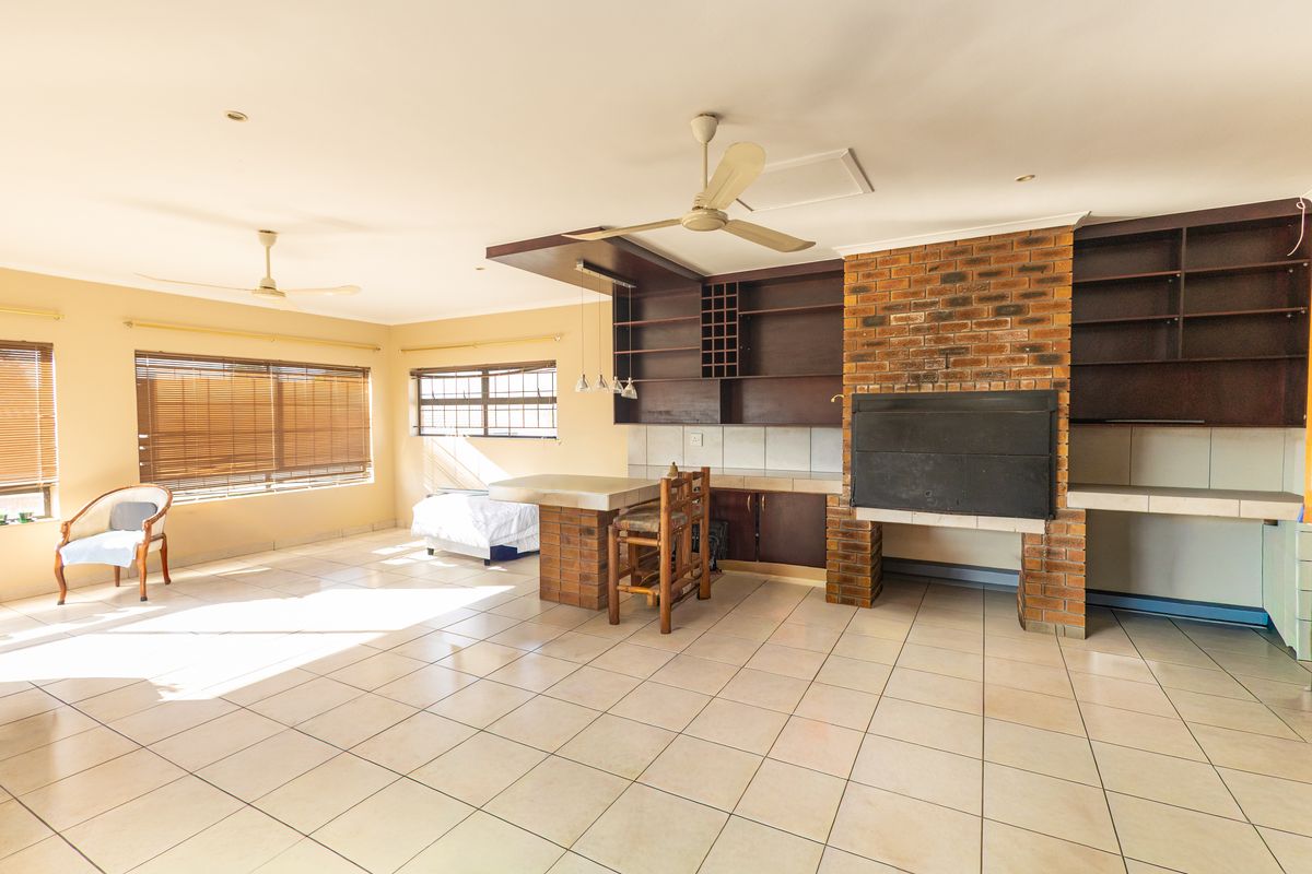Spacious living area featuring a prominent built-in brick fireplace, integrated shelving, tiled flooring, and dual ceiling fans, offering a versatile layout for entertainment.