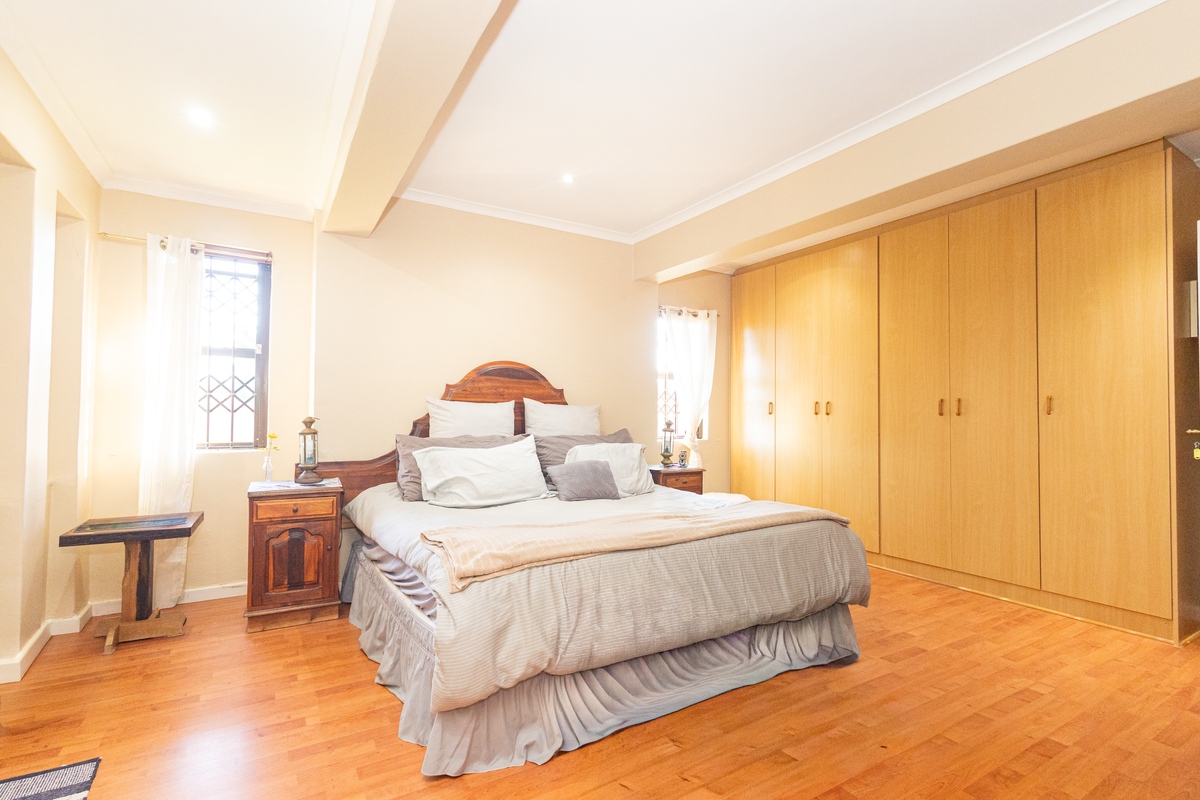 Spacious bedroom featuring extensive built-in wooden cupboards, laminate flooring, and natural light through windows with security bars.