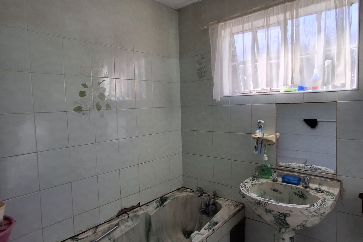 A dated bathroom featuring a pedestal basin and built-in bathtub with original tiled finishes, requiring significant renovation and modernization.