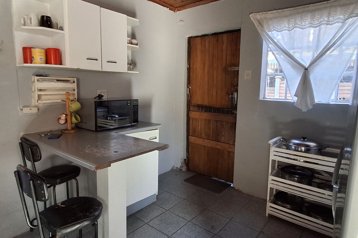 A compact kitchen featuring tiled flooring, timber ceiling, built-in cabinetry, and a breakfast counter, offering a functional space with potential for modernization.