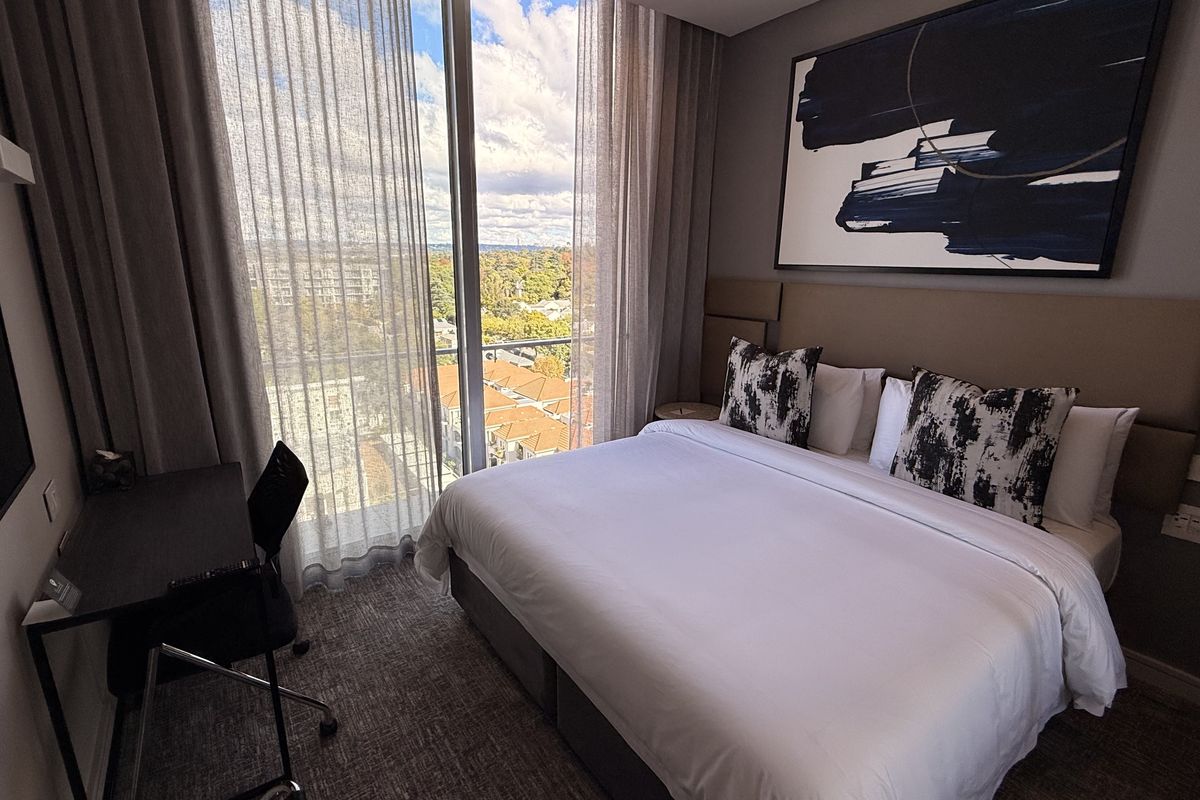 Modern bedroom featuring floor-to-ceiling windows with city views, an integrated upholstered headboard, and neutral finishes in a contemporary penthouse setting.