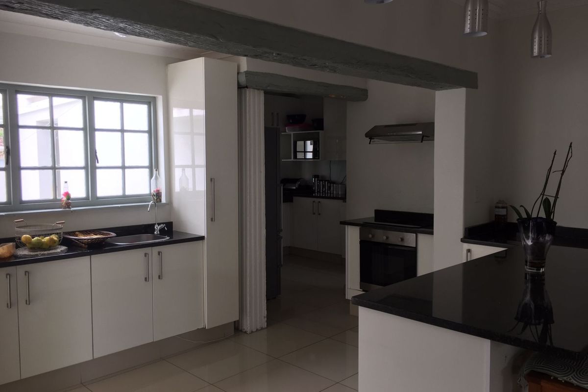 Modern kitchen featuring white cabinetry, dark granite countertops, tiled flooring, and a separate scullery area with built-in oven and extractor fan.