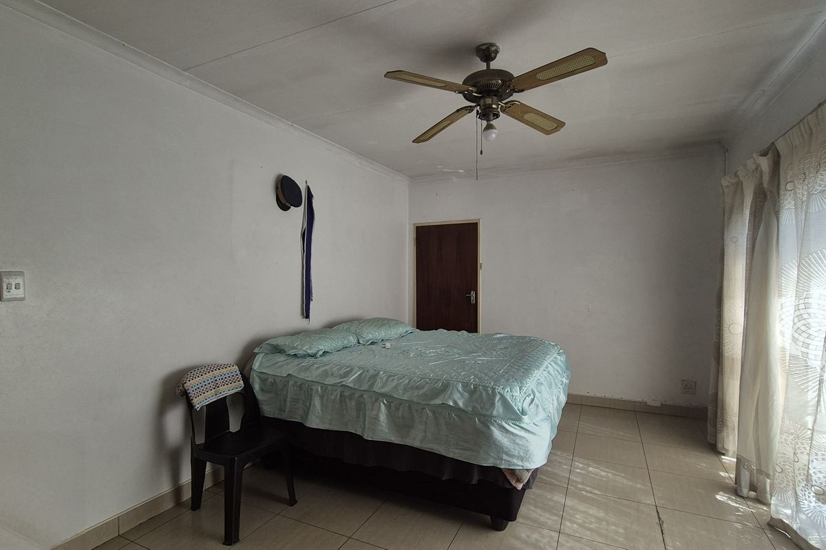 A bedroom featuring tiled flooring, a ceiling fan, and large windows with curtain rails, requiring cosmetic updates to improve its overall condition.