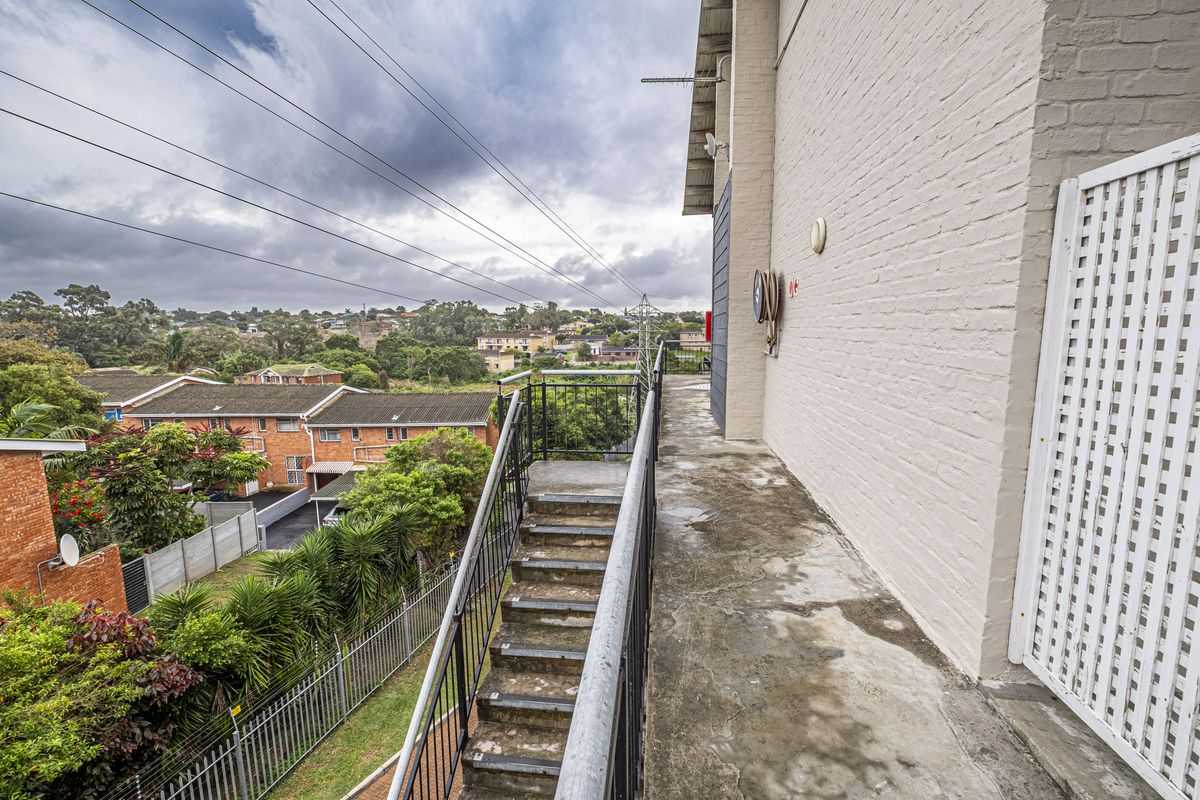 An exterior rear walkway featuring a metal staircase, concrete flooring, and painted brick facade overlooking the surrounding residential neighborhood.