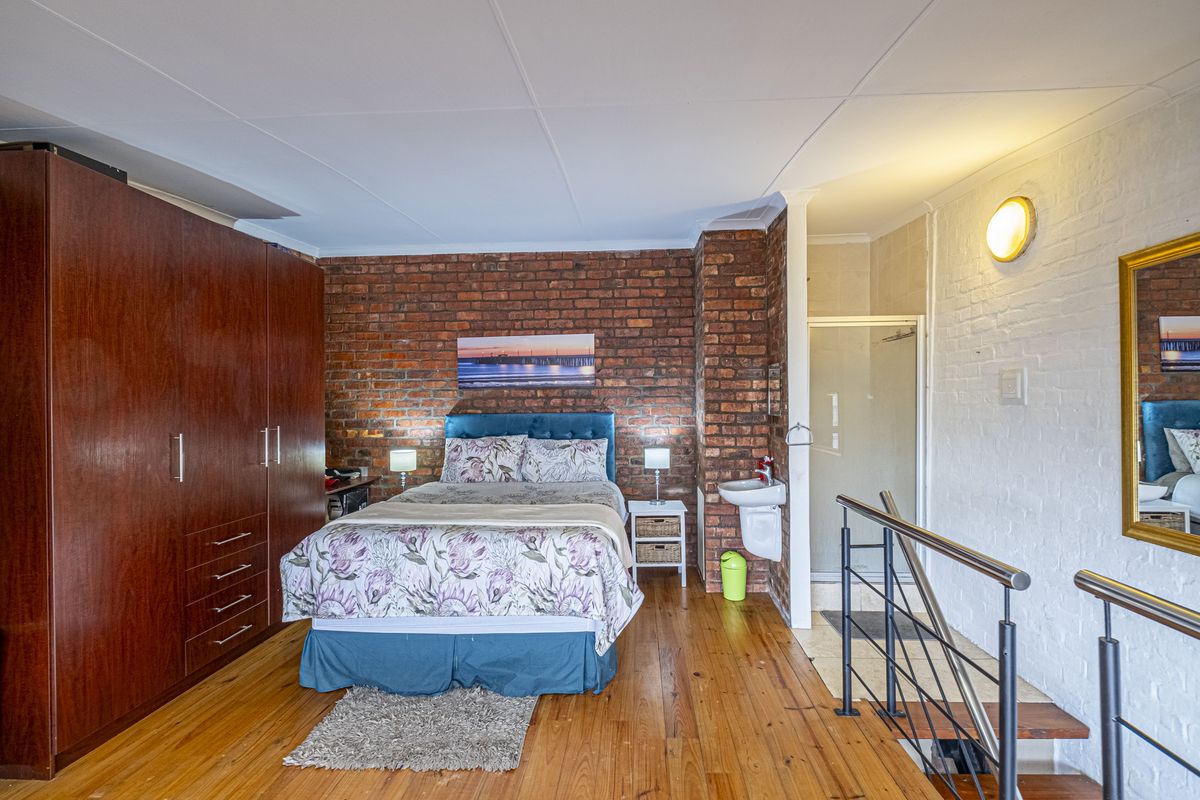 Bedroom featuring exposed brickwork, timber flooring, built-in cabinetry, and an integrated en-suite shower and basin area.