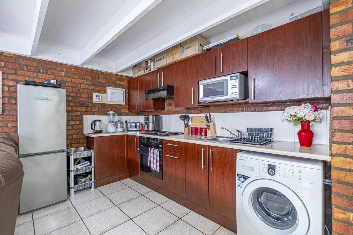 A functional kitchen featuring dark wood cabinetry, exposed brick walls, tiled flooring, and integrated appliances including an oven, hob, and extractor fan.