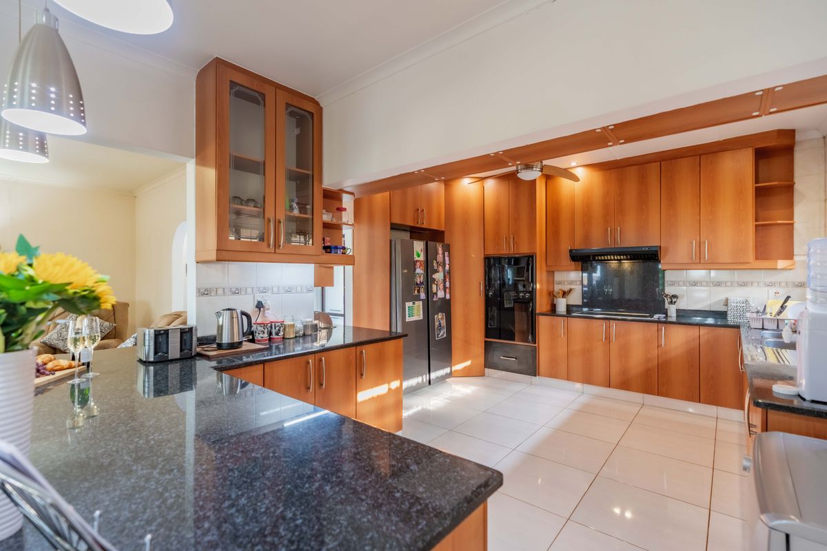 Spacious kitchen featuring warm wooden cabinetry, dark granite countertops, built-in oven, extractor fan, and light-colored floor tiles, offering a functional and classic layout.