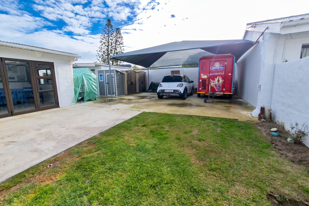 Rear exterior area featuring a concrete driveway with a shade sail, boundary walls, and access to the main dwelling via sliding doors.