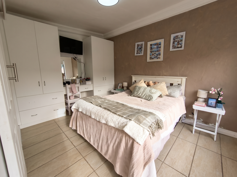 A well-lit bedroom featuring built-in white wardrobes, neutral tiled flooring, and a decorative accent wall with crown molding.