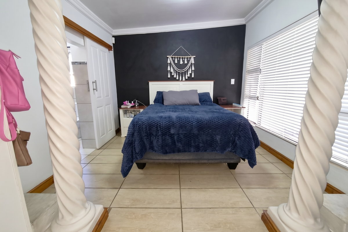 A well-maintained bedroom featuring decorative columns, tiled flooring, and a sliding door leading to an en-suite bathroom.
