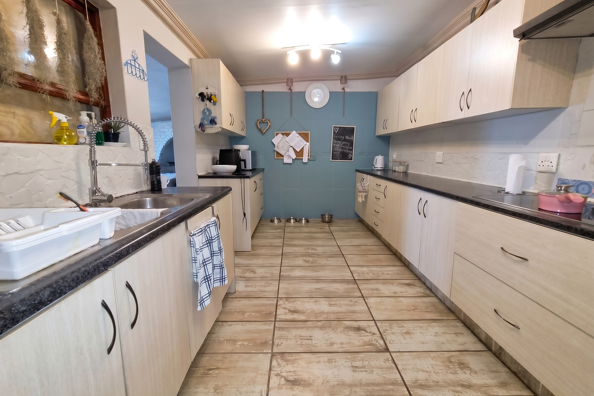 A functional galley-style kitchen featuring light wood-grain cabinetry, dark laminate countertops, ceramic floor tiles, and a modern gooseneck sink faucet.