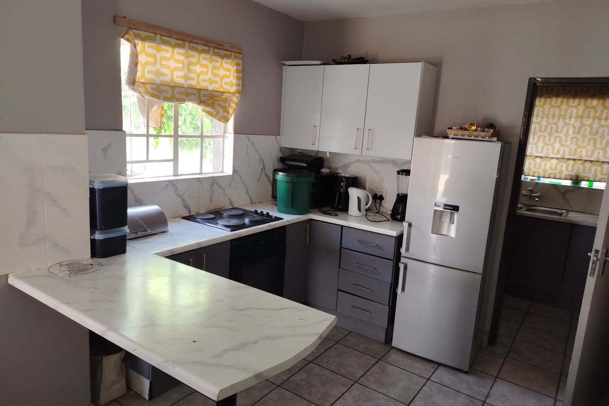 A functional kitchen featuring grey and white cabinetry, marble-effect countertops, a built-in hob and oven, and tiled flooring.