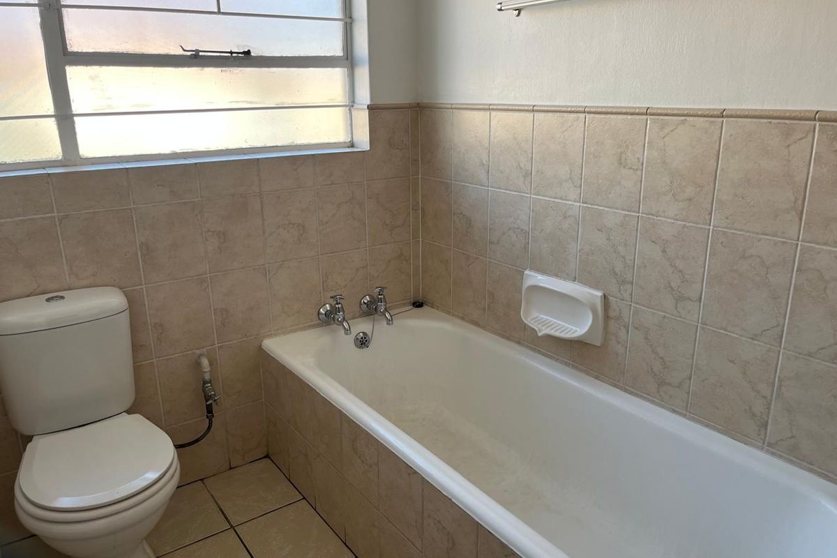 A functional bathroom featuring a standard bathtub, toilet, and neutral wall and floor tiling with a window for natural light.