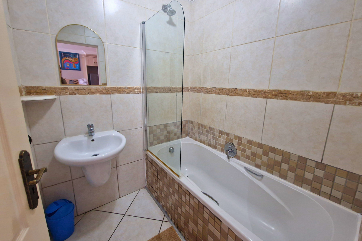 A functional bathroom featuring a wall-mounted basin, a bathtub with a glass shower screen, and neutral tiled finishes with a decorative mosaic border.