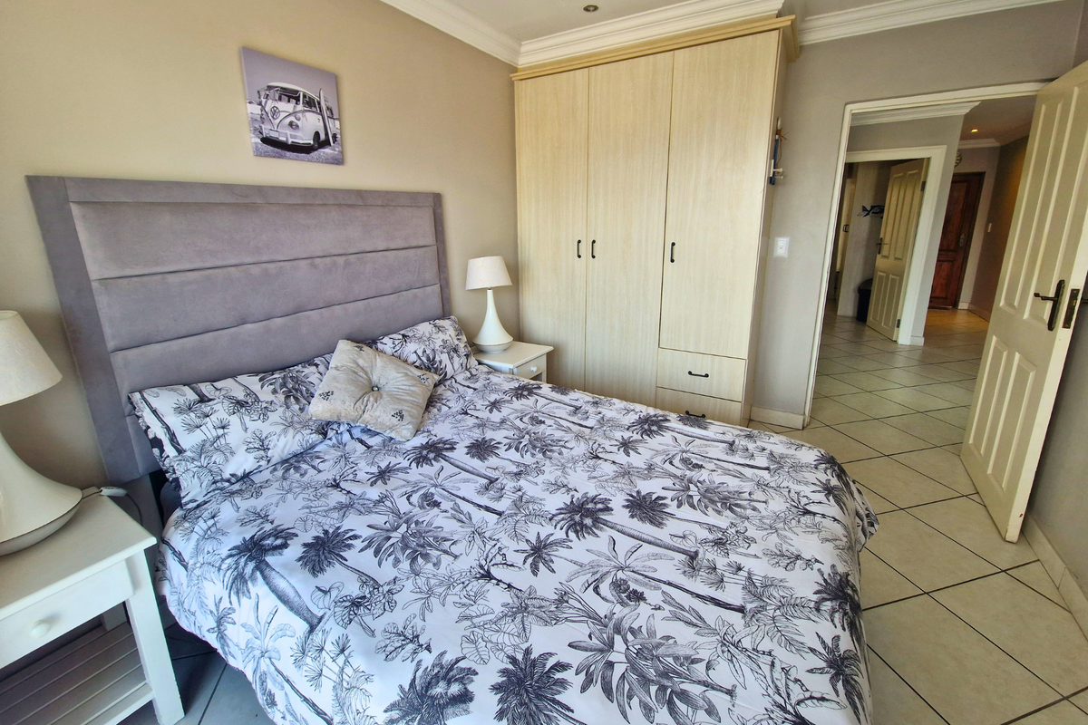 A well-maintained bedroom featuring built-in wardrobes, tiled flooring, and crown molding, with an open doorway leading to the hallway.