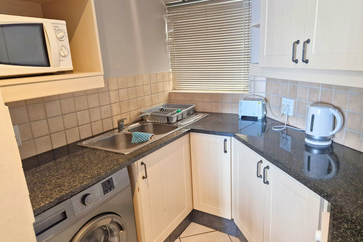 Compact kitchen featuring granite countertops, a stainless steel double sink, tiled backsplash, and built-in cabinetry with a dedicated microwave shelf.