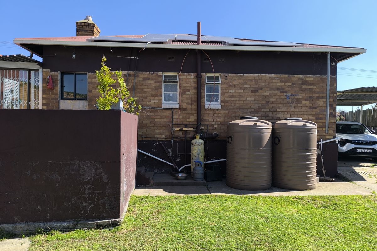 Rear view of the property featuring a brick facade, roof-mounted solar panels, and two large water storage tanks situated on a concrete base.