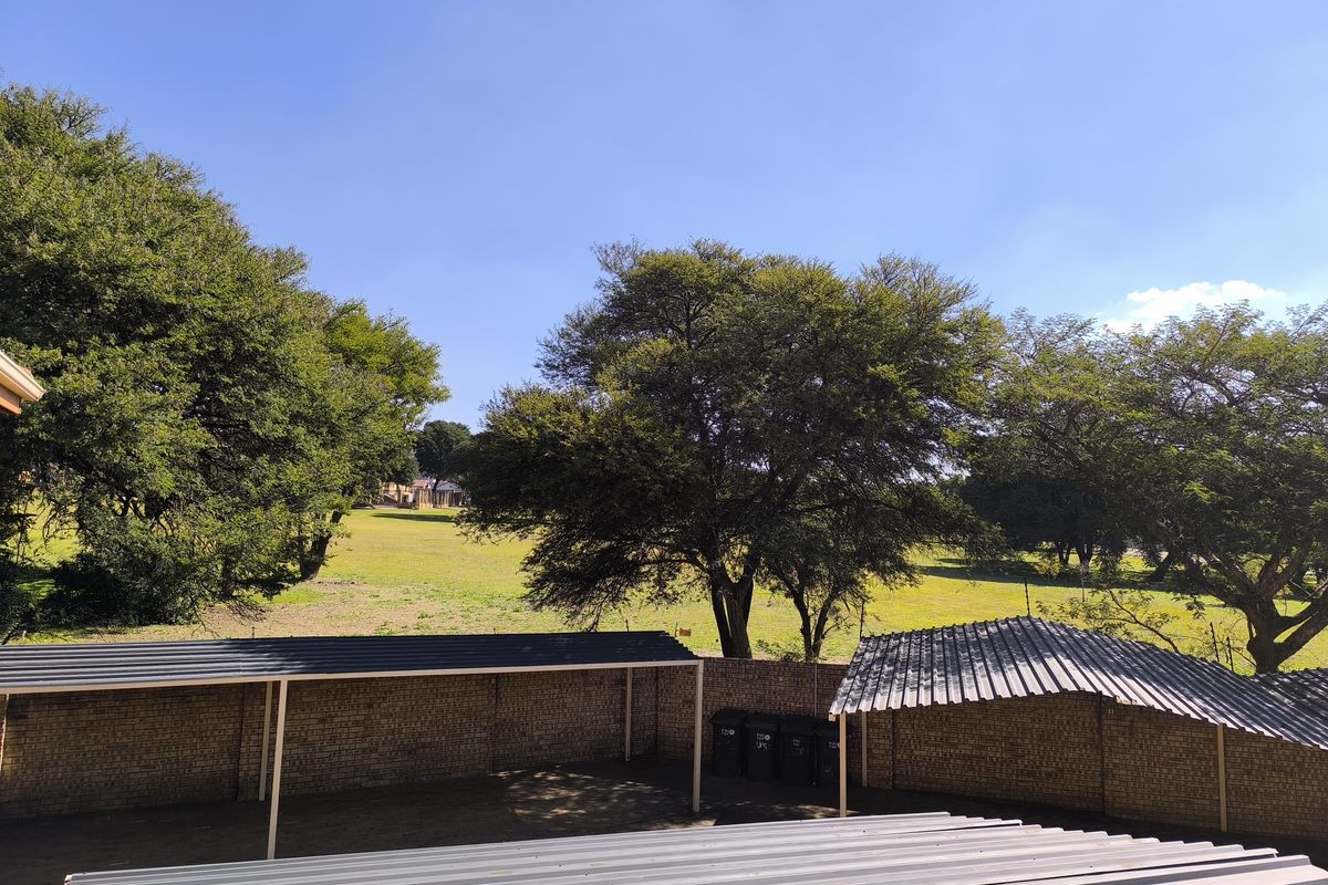 An elevated view of a rear parking area featuring covered carports with corrugated metal roofing and brick boundary walls overlooking a grassy field.