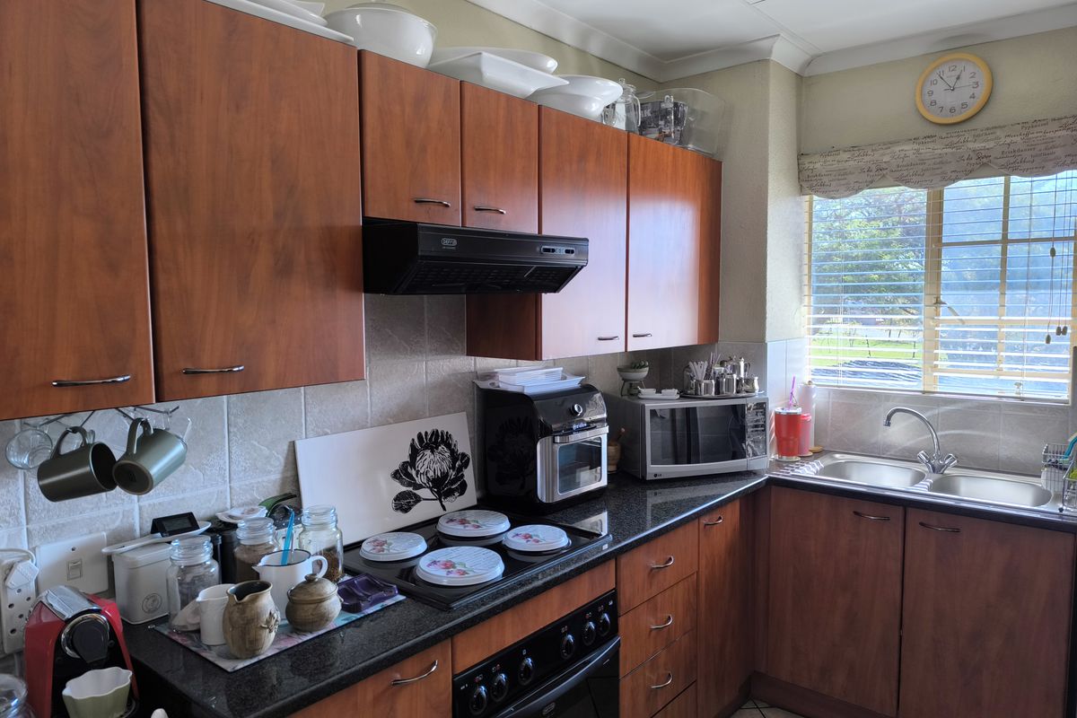 A functional kitchen featuring wood-look laminate cabinetry, granite countertops, a built-in oven with hob, and a double bowl sink with a tiled backsplash.
