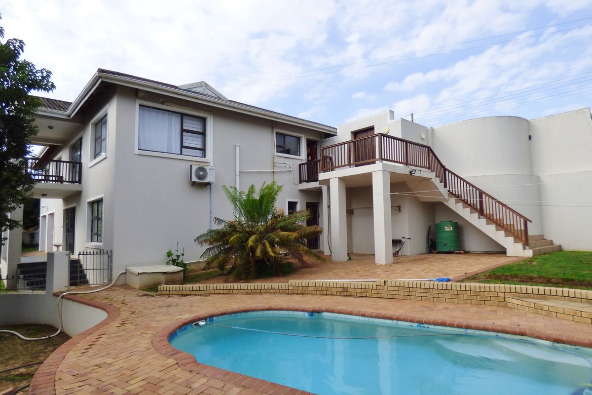 Rear exterior view featuring a swimming pool, brick paved patio area, and an external staircase leading to an upper level balcony.