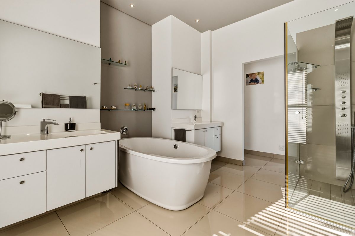 Modern bathroom featuring a freestanding bathtub, double vanity with storage, and a glass-enclosed shower with a contemporary wall-mounted shower panel.