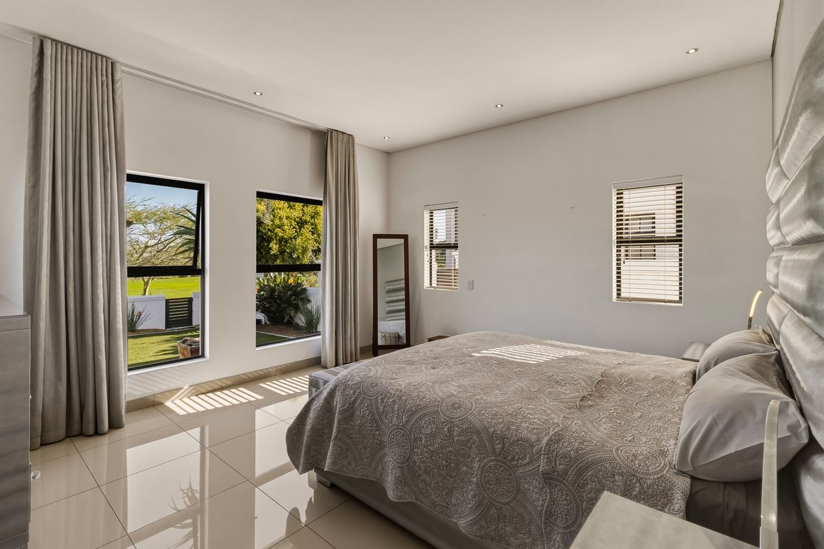 Spacious bedroom featuring polished tiled flooring, recessed downlights, and large windows with integrated blinds and curtain tracks, offering views of the garden.