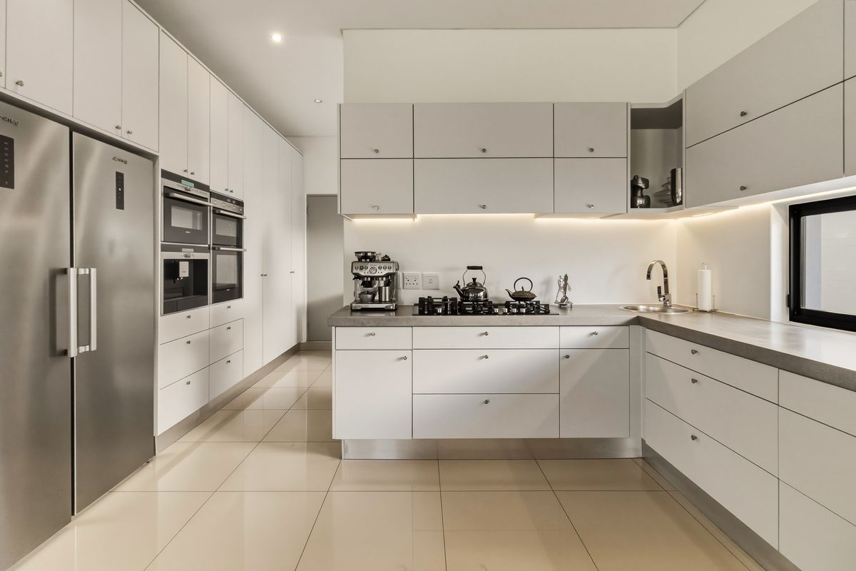 Modern kitchen featuring sleek white cabinetry, stone countertops, integrated appliances, gas hob, and under-cabinet lighting with polished tiled flooring.
