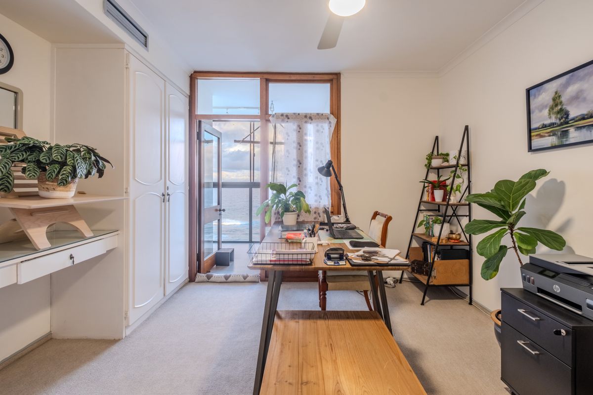 A functional bedroom featuring built-in wardrobes, ducted air conditioning, and direct access to a balcony with ocean views.