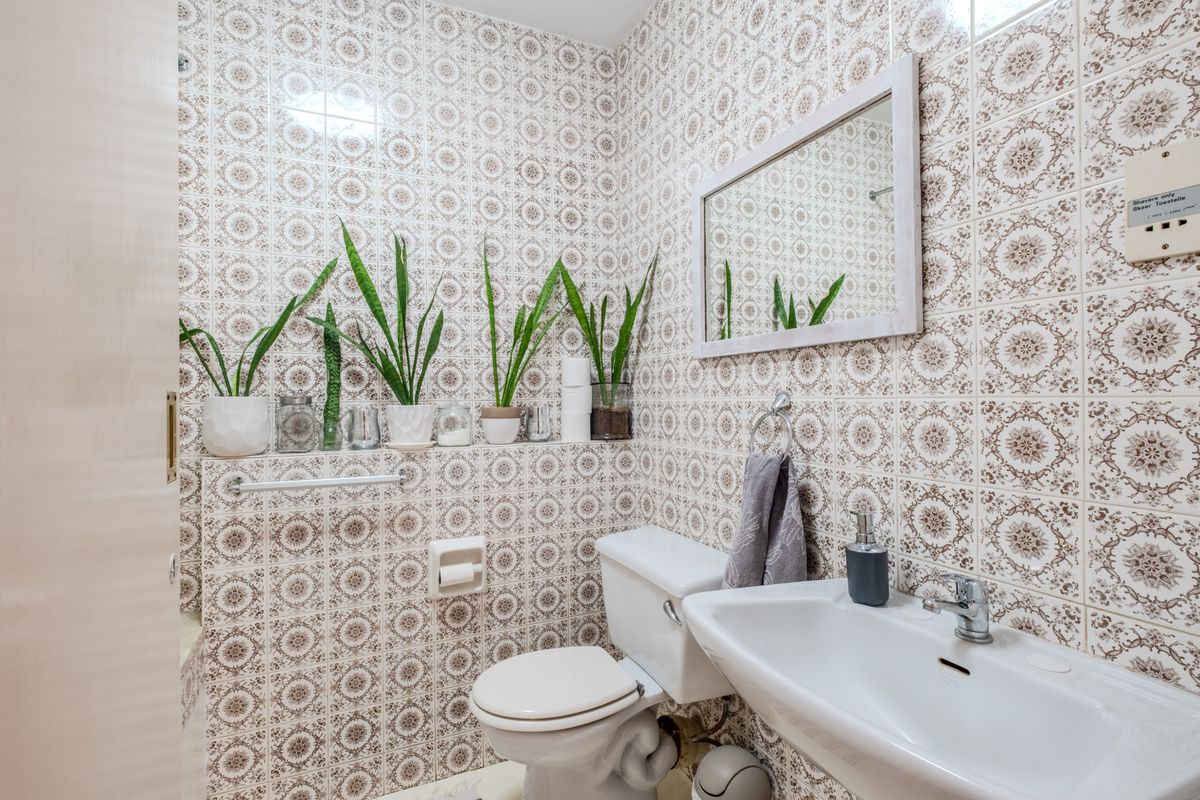 A compact bathroom featuring vintage-style patterned ceramic wall tiles, a white pedestal washbasin, and a standard toilet.