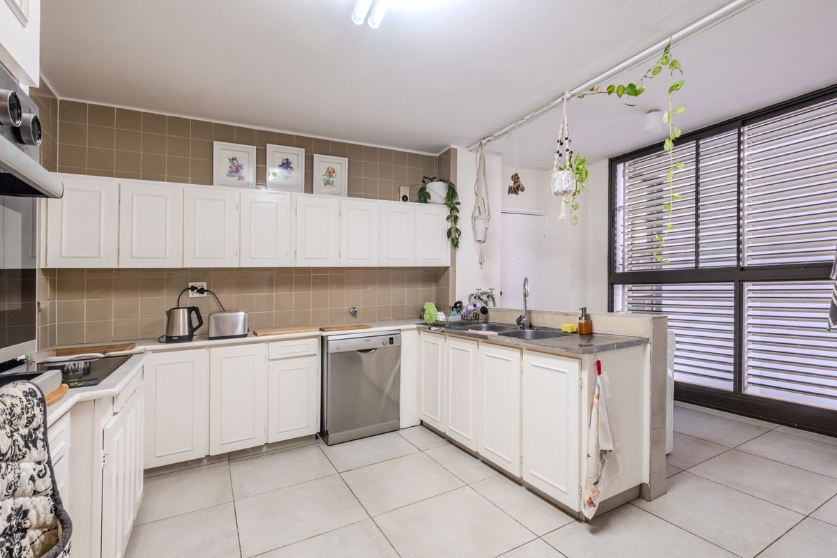 A functional kitchen featuring white cabinetry, tiled backsplash, and tiled flooring, with a large window providing natural light and ventilation.