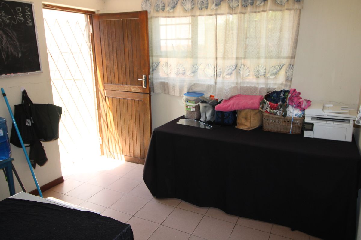 A bedroom featuring tiled flooring, a timber door with a security gate, and a window, currently used as a multi-purpose space.