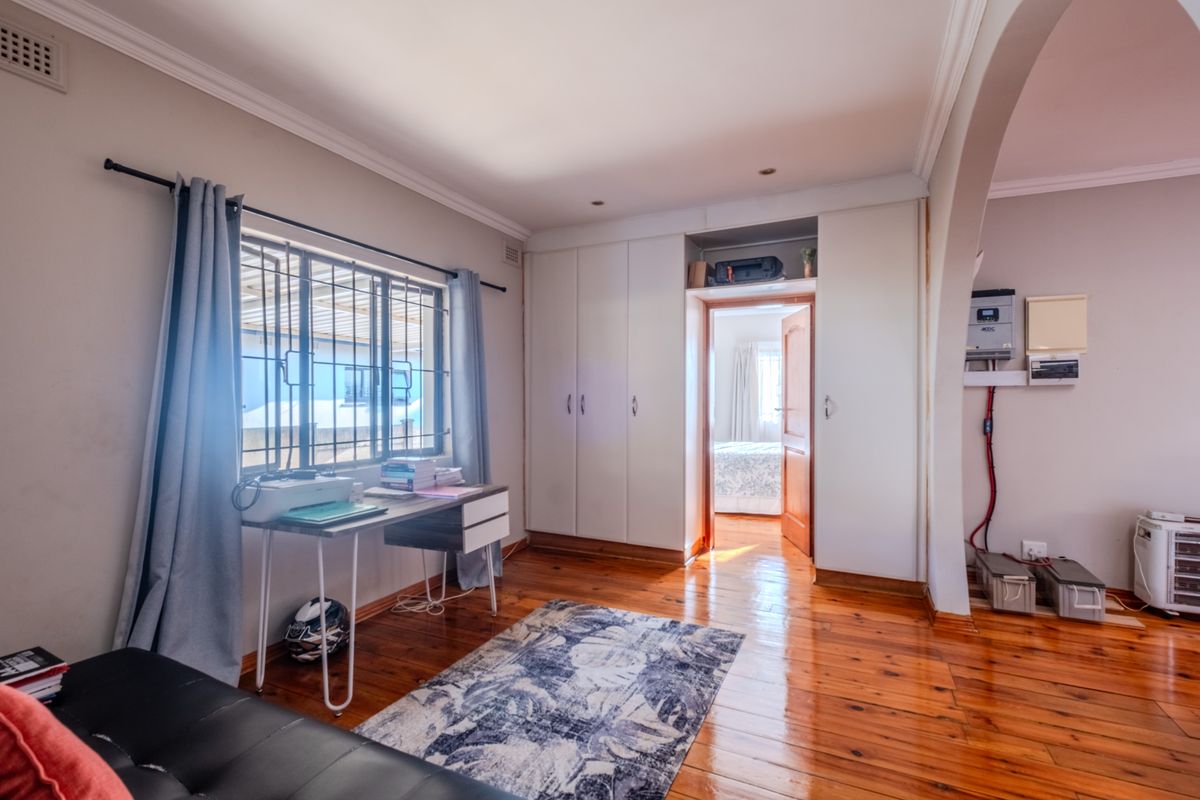 A bedroom featuring polished timber flooring, built-in cupboards, and an integrated inverter system, with natural light entering through a window with security bars.