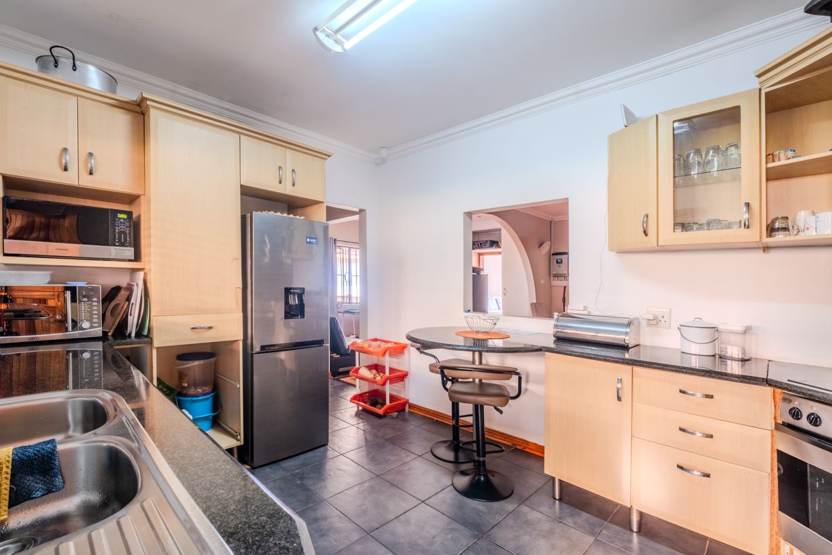 Functional kitchen featuring light wood cabinetry, granite countertops, built-in oven and hob, and a convenient breakfast bar area with tiled flooring.