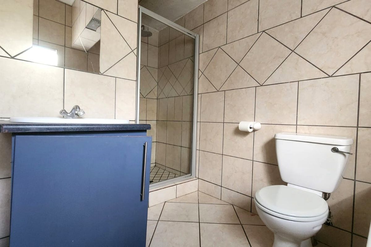 A functional bathroom featuring a vanity with basin, a glass-enclosed shower, and a standard toilet, finished with neutral wall and floor tiling.