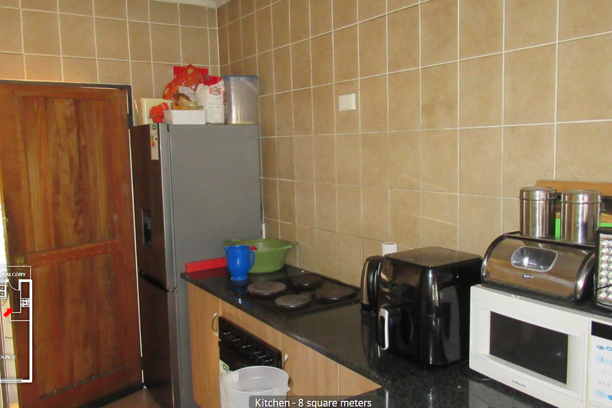 Compact kitchen featuring laminate cabinetry, stone countertops, and tiled splashbacks, providing a functional workspace with direct access to the balcony area.