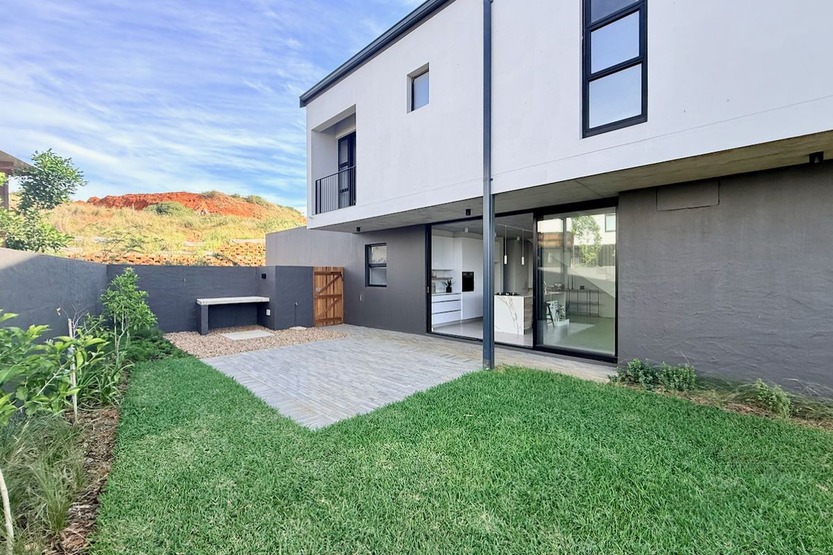 Modern rear exterior featuring a paved patio, built-in braai area, and a well-maintained lawn with direct access to the interior through sliding glass doors.