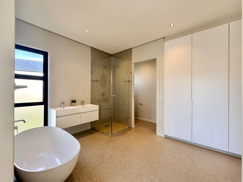 Modern bathroom featuring a freestanding bathtub, wall-mounted double vanity, glass-enclosed shower, and ample built-in storage cabinetry.
